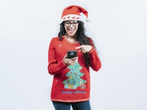 Happy girl in Christmas sweater looking pointing phone screen, isolated