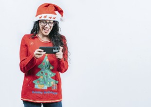 Surprised girl in Christmas sweater looking at cell phone screen, isolated. Surprised girl in