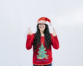 Smiling girl in Christmas hat pointing up isolated. Beautiful girl in Christmas sweater showing and