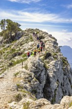Group of people mountain hiking on a path by a steep rock in a mountainous landscape a sunny summer