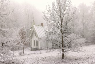 White wooden residential house in a park landscape with hoarfrost on the trees and new snow on the