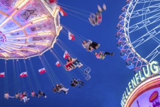 Rotating chain carousel at night at a funfair with floating people in front of a deep blue sky, Bad