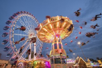 An illuminated chain carousel and Ferris wheel at night at a funfair, people swinging on chains,