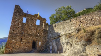 Lower main entrance, Historic ruins with flags in front of stony terrain under blue sky, Mystras,