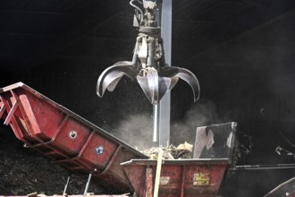 Loading crane with grab arm for loading wood waste for wood pellet production on the premises of