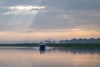 Motorboat on the lake, morning mood, reflection in Lake Victoria, sunbeams and cloudy sky, Mabamba