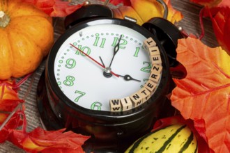 Winter time changeover: close-up of an alarm clock, autumnal decoration and letter cubes displaying