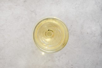Close-up overhead view of a glass filled with white wine on a light textured surface