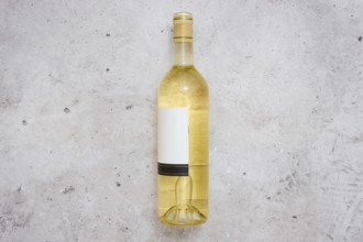 A white wine bottle with a blank label on a light grey textured surface. The setting suggests a