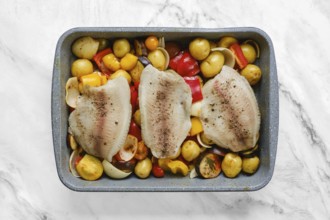 Fish fillets on a bed of colorful roasted vegetables, including onions, peppers, and baby potatoes