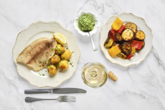 Grilled fish fillet with tender baby potatoes garnished with herbs, alongside a bowl of vibrant