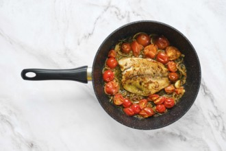 A frying pan holds a seasoned fish fillet surrounded by bright cherry tomatoes. The scene captures