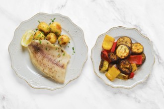 A beautifully plated dish features grilled white fish alongside tender baby potatoes and a colorful