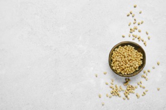 A wooden bowl filled with golden pine nuts on a light gray textured surface. Some nuts are