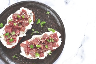 Sandwiches, rye bread with cream cheese, sliced tuna fillet with herbs, breakfast on a black plate,
