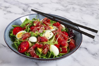 Salad with fresh tuna, cherry tomatoes and quail eggs and avacado, served with chopsticks