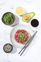 Fresh tuna tartare with avocado served on a marble table with soy sauce and seaweed salad
