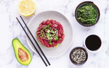 Fresh tuna tartare with avocado served on a marble table with soy sauce and seaweed salad
