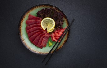Fresh tuna sashimi served with lemon, wasabi, and pickled ginger on a dark background