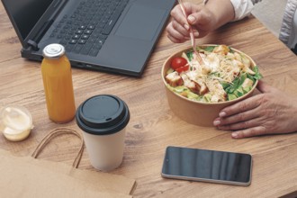 A woman is working on a laptop at home, there is food on the table, salad, coffee and juice,