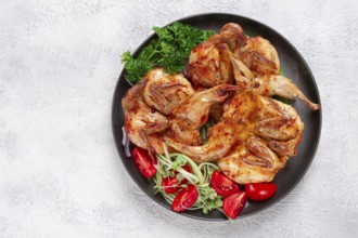 Baked quail, served on a plate with crispy lettuce leaves, fresh tomatoes and herbs, on a dark