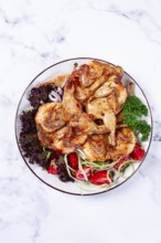 Baked quail, served on a plate with crispy lettuce leaves, fresh tomatoes and herbs, on a white