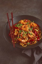 Udon stir-fry shrimp noodles with red bell pepper and green onion, served in a black bowl, with