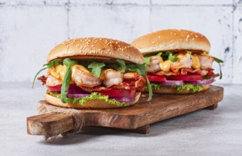 Two shrimp burgers and buns with sesame seeds, bacon, lettuce, tomatoes and onions, On a wooden