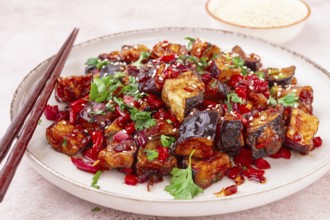 Fried eggplant, Chinese style, in sweet and sour sauce, with pepper and sesame seeds. on a white