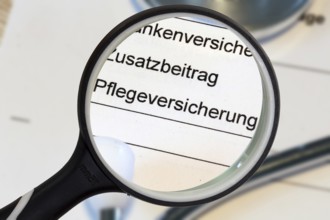 (Photomontage) Close-up of the word PFLEGEVERSICHERUNG on a document, enlarged with a magnifying