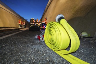 A yellow fire hose lies on the ground, with firefighters in the background, fire drill in the new