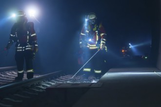 Firefighters working on railway tracks at night with torches and safety equipment, firefighting