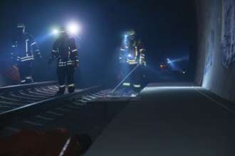 Three firefighters walking along a tunnel wall, torch lit, fire drill in the new tunnel of the