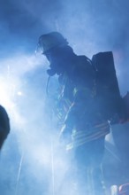 Firefighter in smoke with breathing apparatus and helmet, blue light surrounding him, fire drill in