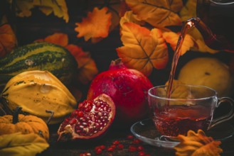 Tea is poured into a glass cup, pomegranate and pumpkins, autumnal atmosphere