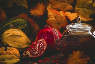 Teapot, pomegranate and pumpkins against a background of autumn leaves