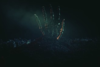 A single skeletonised hand protruding eerily from the dark earth, Halloween