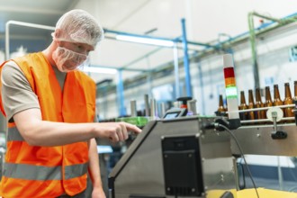 Male worker in protective gear overseeing automated beer bottling and labeling on a clean modern