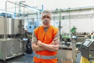 Worker standing proudly with crossed arms, wearing a safety vest and hairnet in a clean, automated