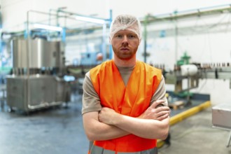 Male worker standing with crossed arms, wearing a hair net and a safety vest, overseeing operations