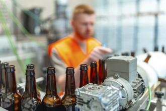 Brown glass bottles moving along a conveyor belt, with a factory worker in an orange vest