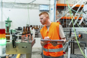Industrial worker wearing safety vest checking quality of bottles on a beverage factory automated
