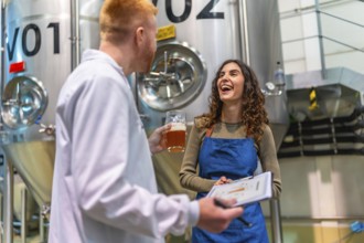 Brewery worker and quality control specialist smiling, holding clipboard and a glass of beer,