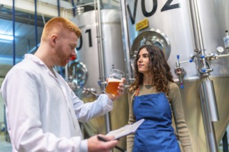 Brewery workers evaluating beer sample for quality control, holding clipboard and glass in brewing