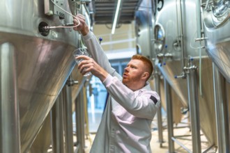 Brewery worker performing quality control, drawing a sample of beer for taste testing and analysis