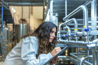 Woman wearing a lab coat meticulously checking industrial pipes and valves in a modern beverage