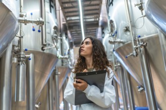 Woman in laboratory coat conducting quality control inspection in a modern beer brewery, holding a