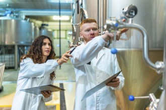Chemical engineers and a quality control technician are checking stainless steel fermentation tanks