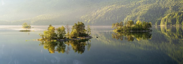 Morning atmosphere at the Eibsee lake, small islands in the first light are reflected in the water,