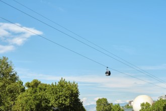 A cable car travels smoothly across a bright sky, suspended over a rich canopy of trees